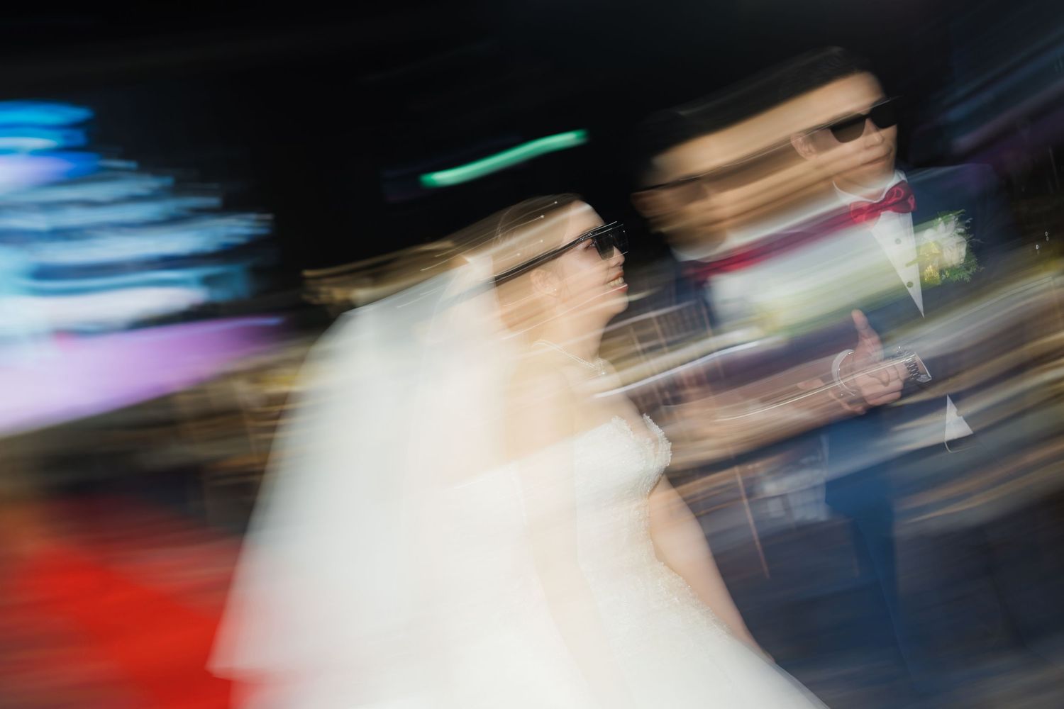 Blurred motion shot of a bride in a white dress walking at night with colorful light streaks in the background.