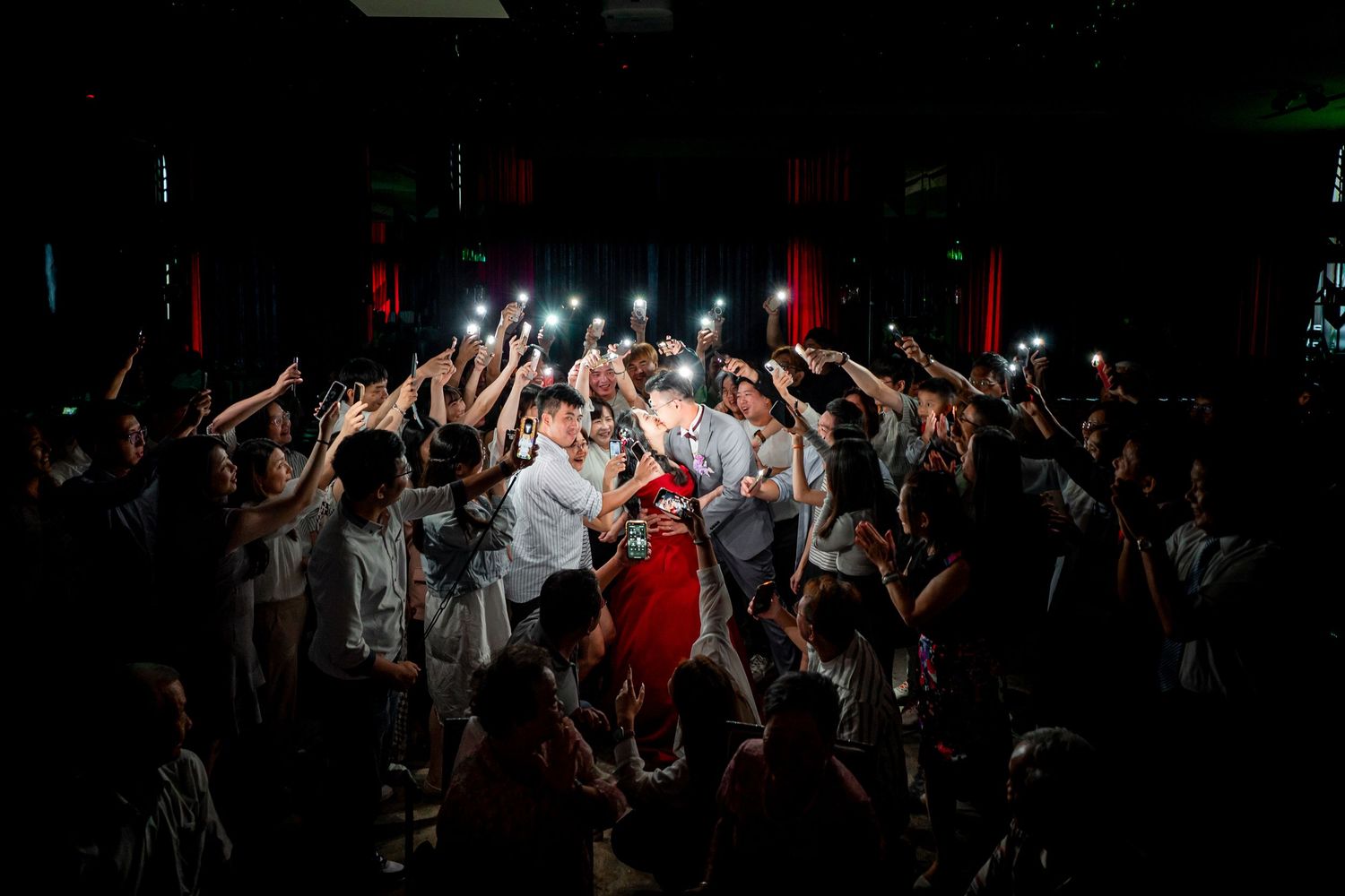 A dark concert venue filled with silhouetted people raising their hands during a live performance.