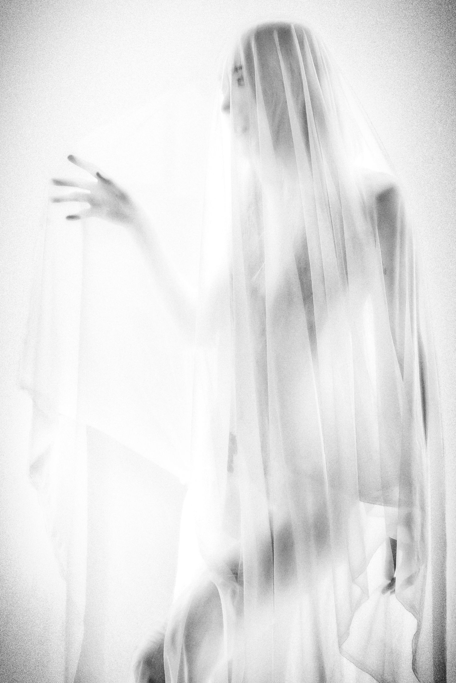 A ethereal figure draped in a flowing white veil, captured in soft black and white photography.