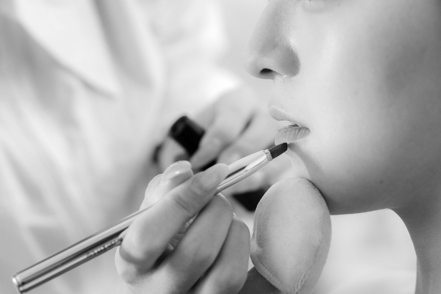 Black and white close-up of a makeup artist applying lip liner to a model's lips with precision.