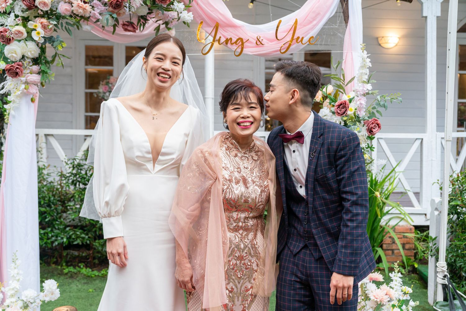Wedding celebration under a floral arch with pink decor and decorative lights in an outdoor garden setting.
