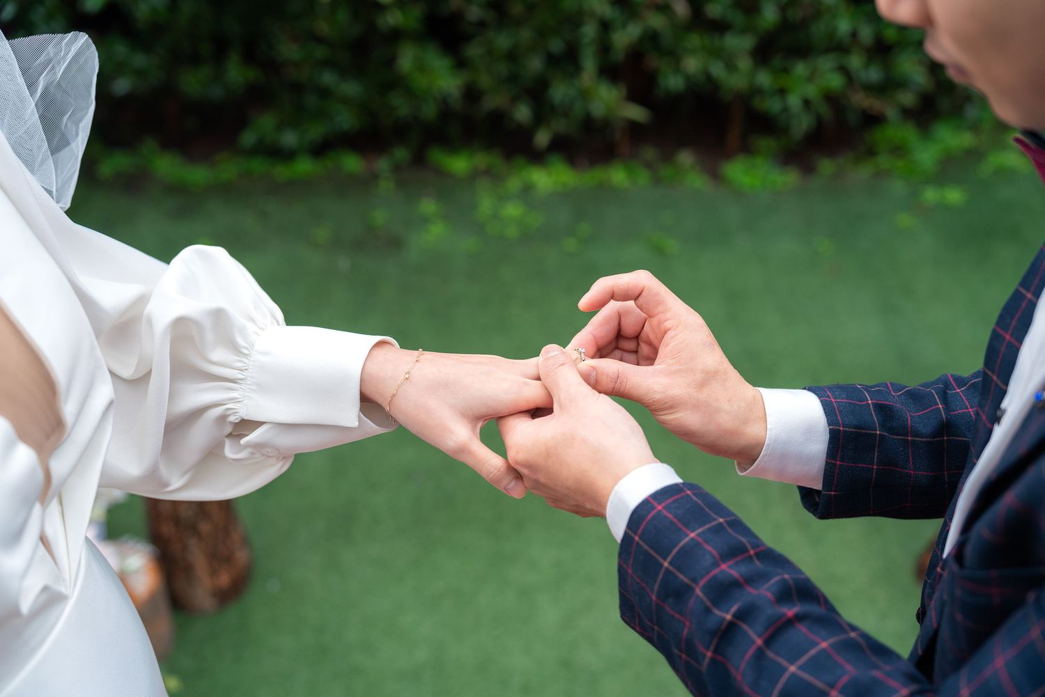 A close-up moment during a wedding ceremony as a ring is being placed on someone's hand outdoors.