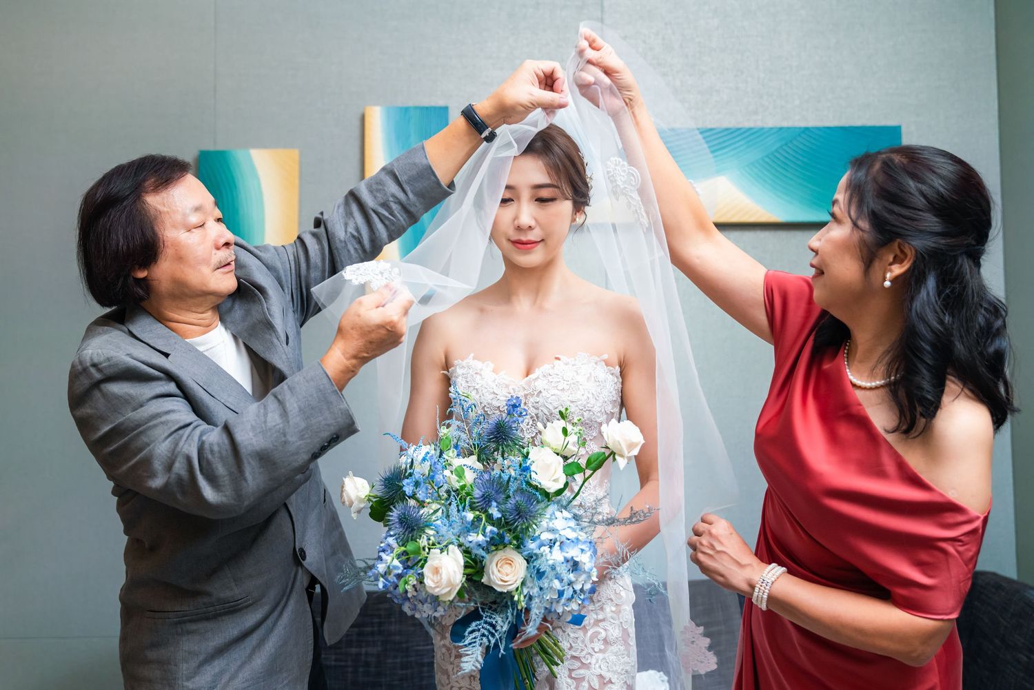 A joyous wedding celebration moment with bridesmaids in grey and red dresses admiring the bride holding blue flowers.