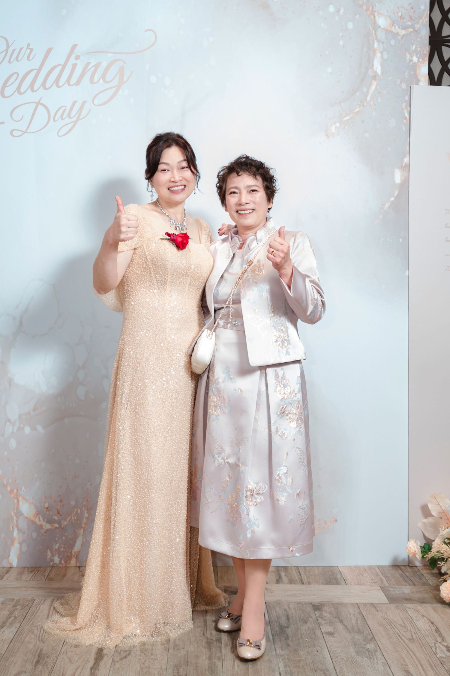 Two people in formal attire pose together against a light backdrop at an elegant celebration.