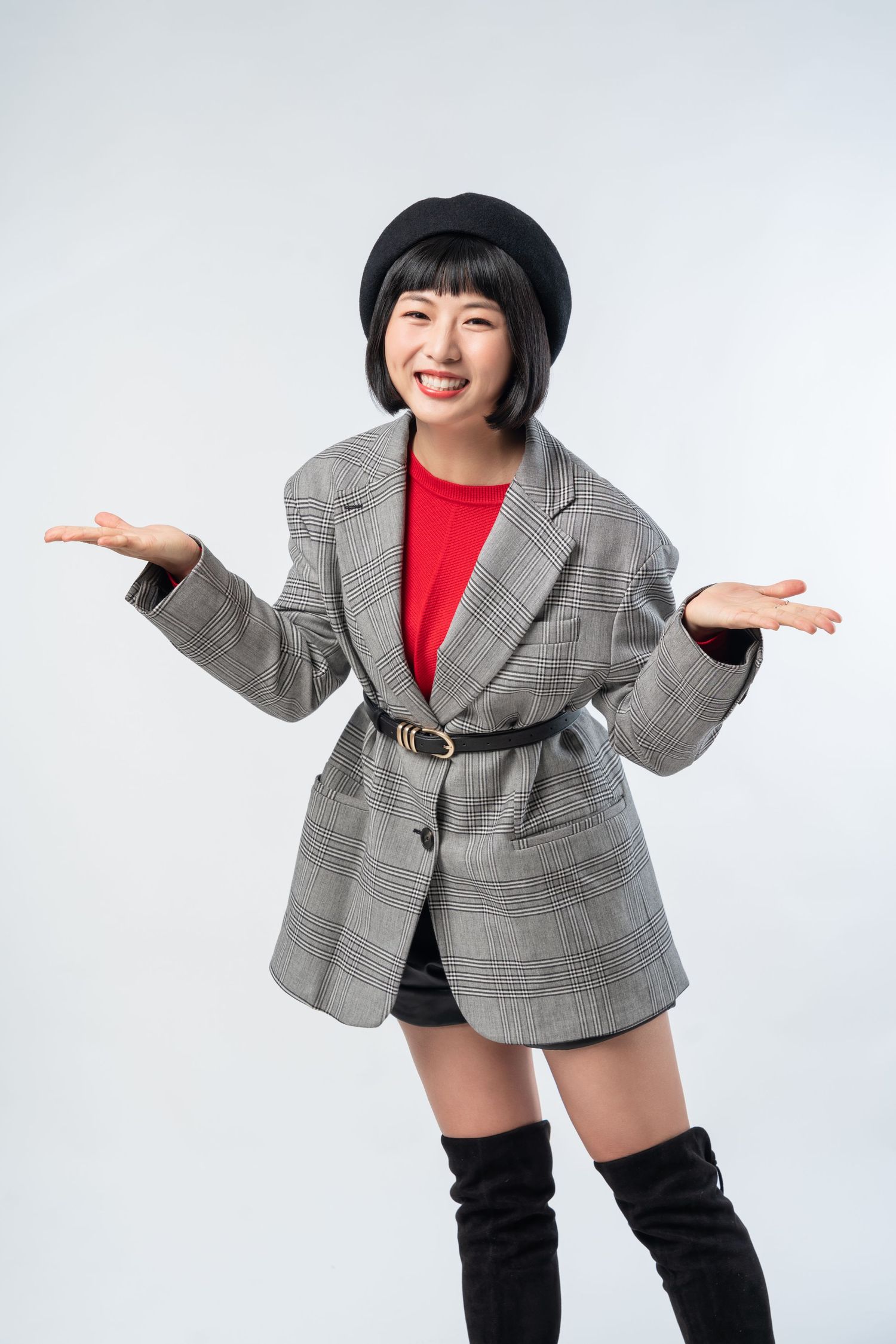 Stylish portrait of someone wearing a plaid blazer, red top, black beret and boots with playful outstretched arms.