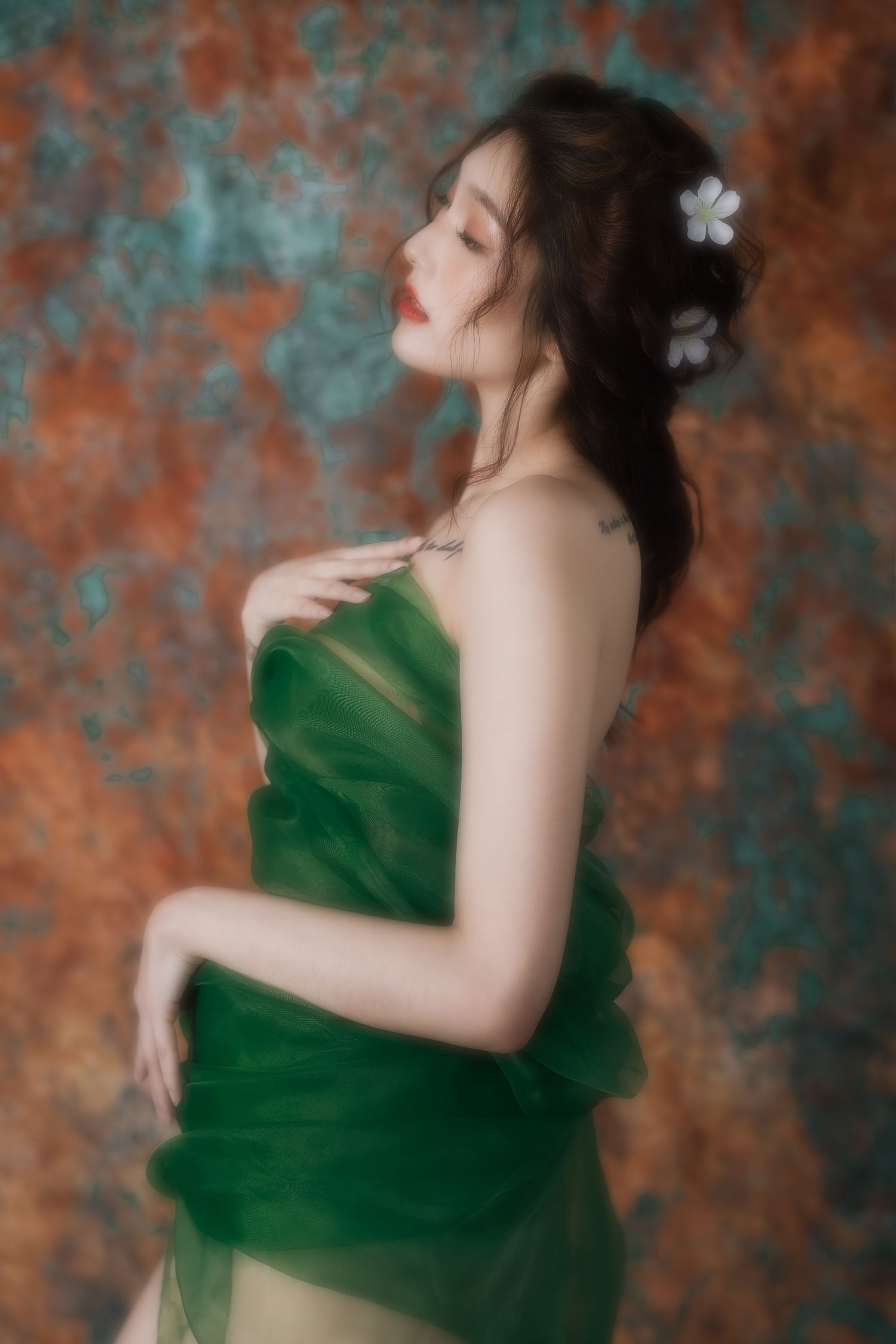 Artistic portrait in emerald green dress against textured orange and teal backdrop with delicate white flowers in dark hair.