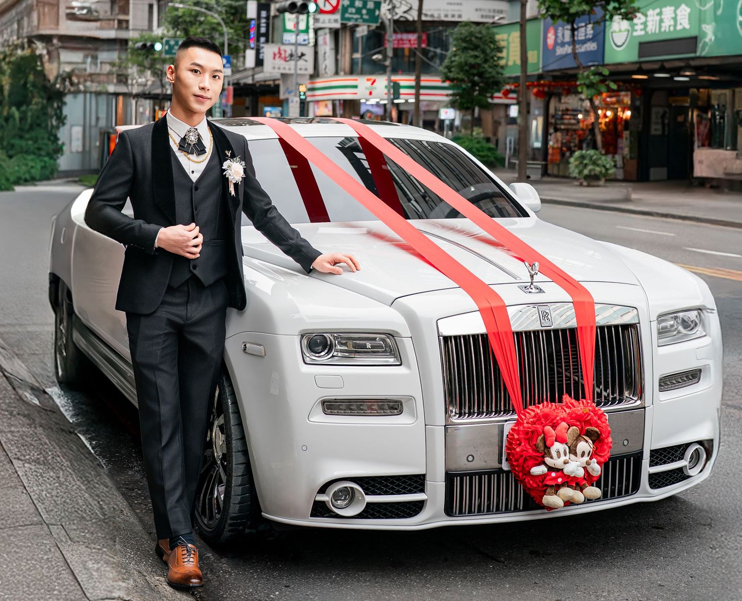 White luxury car decorated with red ribbons for wedding celebration parked on city street.