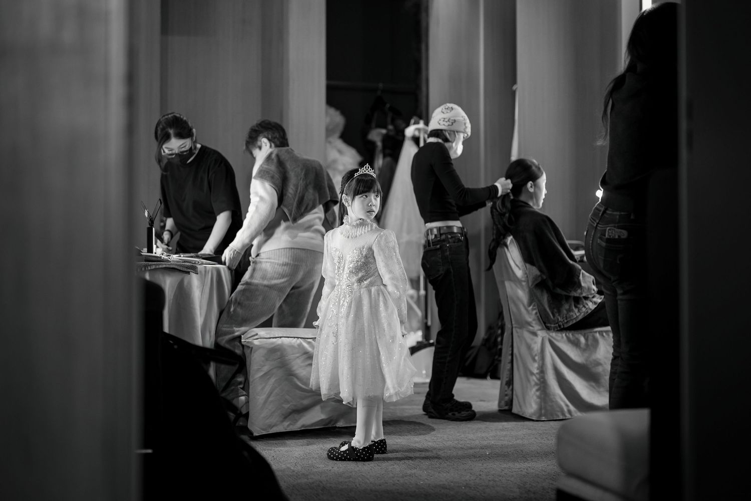 A black and white wedding photograph shows people in formal attire gathered at an elegant indoor venue.