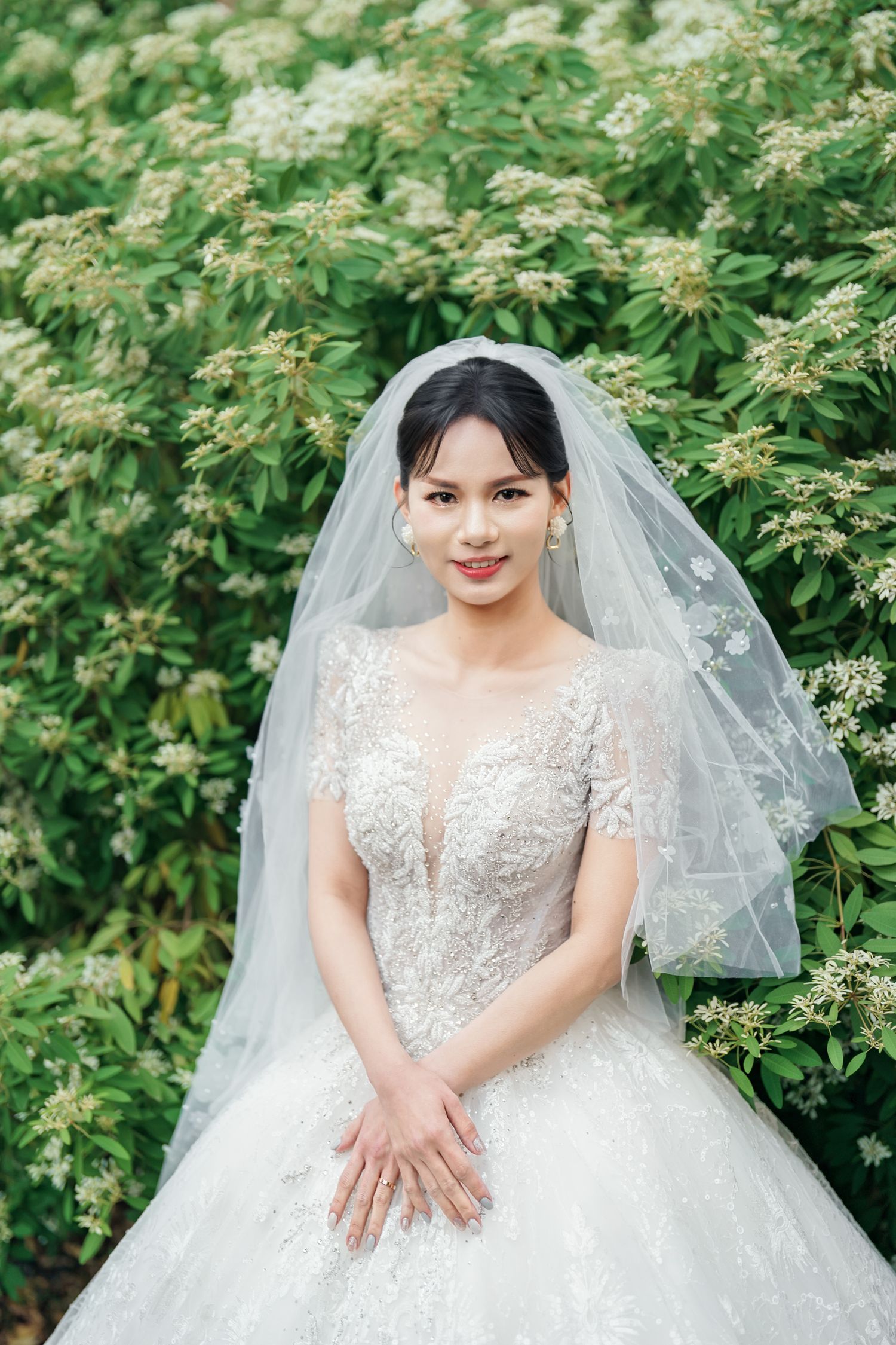 A beautiful wedding dress with delicate lace details and veil captured against lush green foliage.