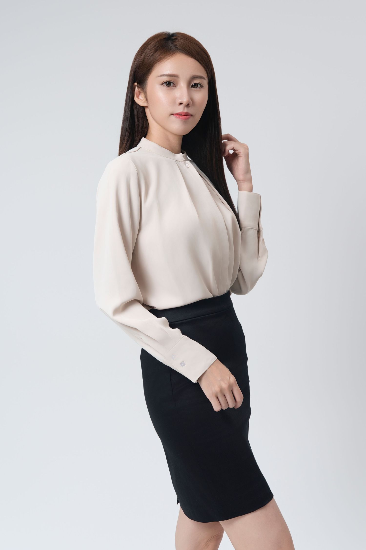 Fashion model wearing cream turtleneck sweater and black high-waisted skirt poses against white background in studio shoot.