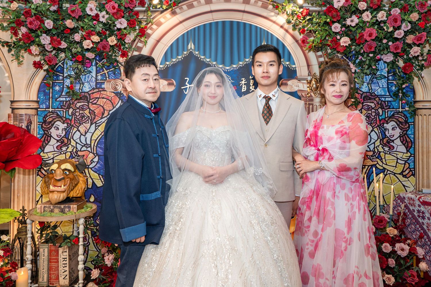 A bride in a white lace gown poses with three family members at an elegant floral wedding venue.