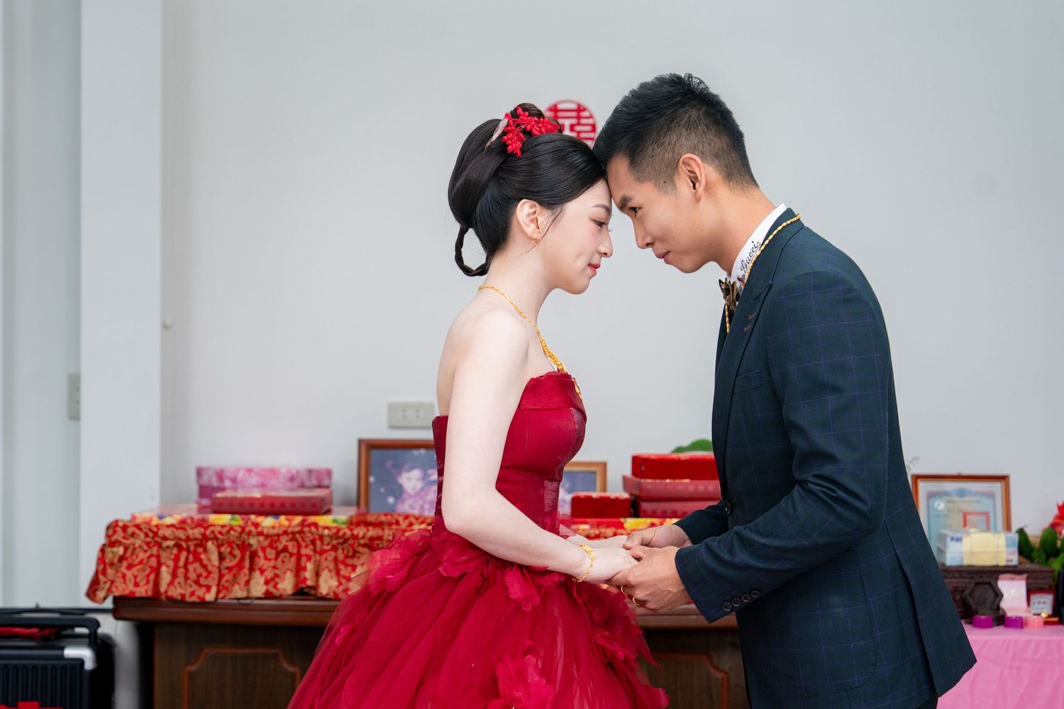 Couple in formal attire sharing an intimate moment, woman in red gown with floral hair accessory, man in navy suit.