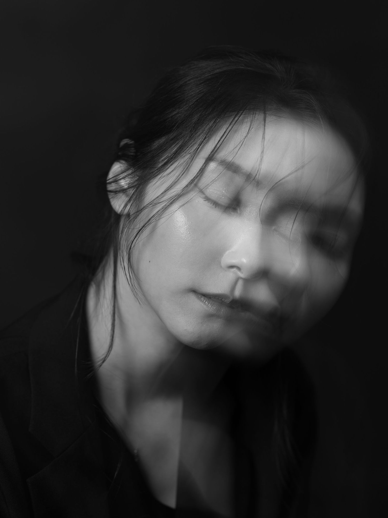 Black and white portrait of a young woman with closed eyes and flowing hair against a dark background.