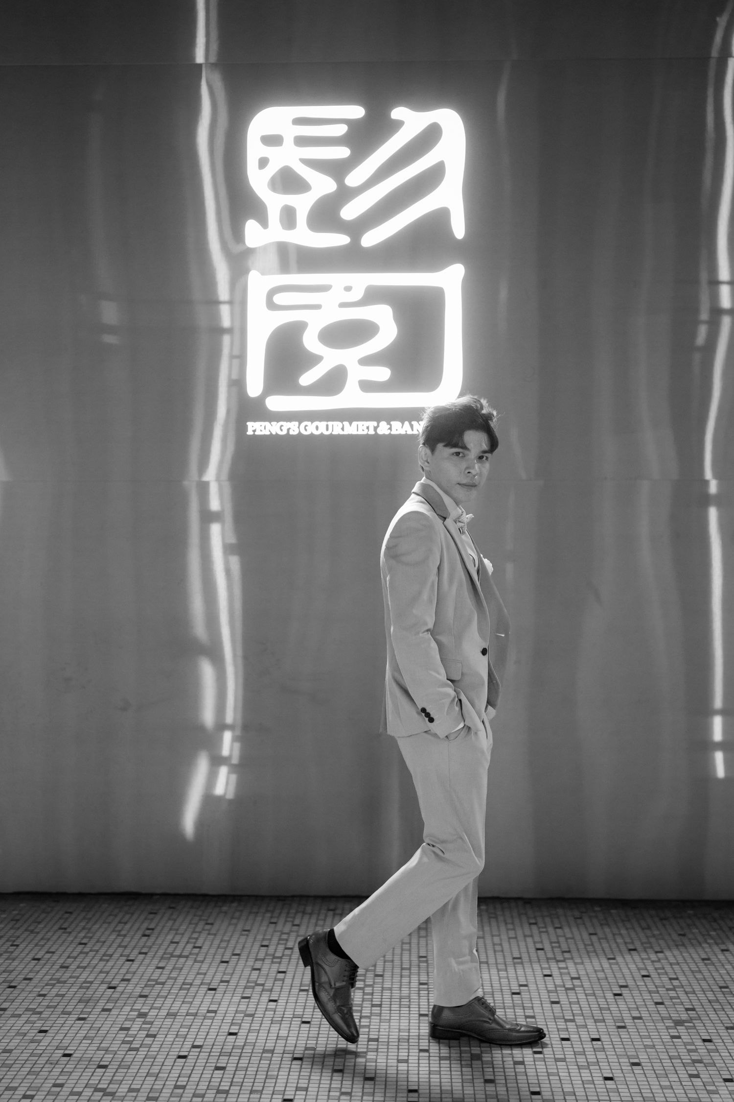 Man in suit posing in front of neon Chinese restaurant sign at Peng's Gourmet & Bar.