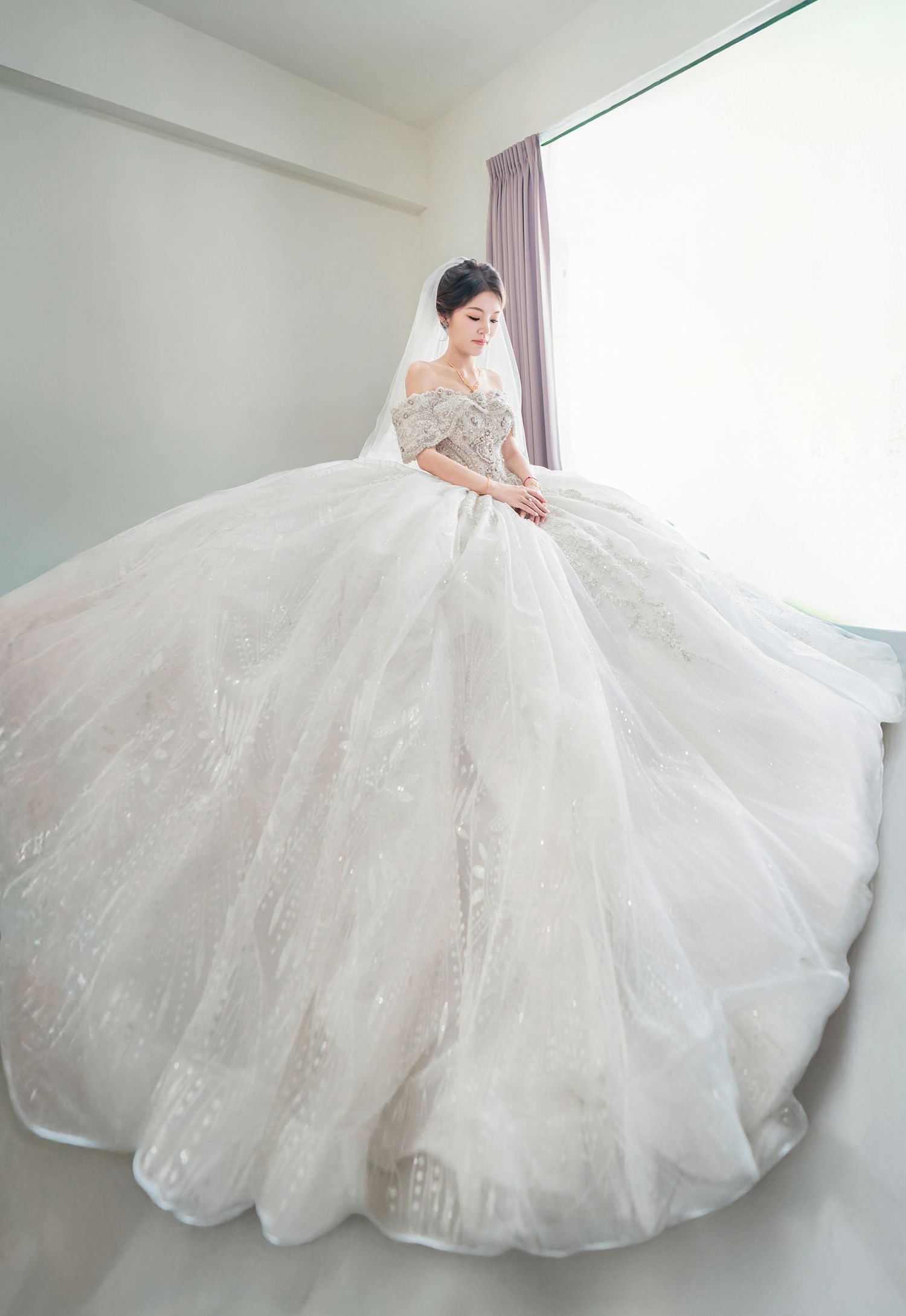 A stunning white ballgown wedding dress with intricate details and a voluminous tulle skirt spreads across a light-colored floor.