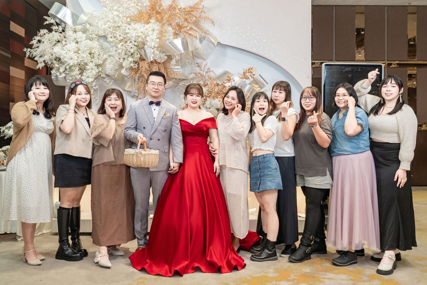 A wedding party poses together in formal attire with bridesmaids in pink and neutral dresses and a bride in a red gown.