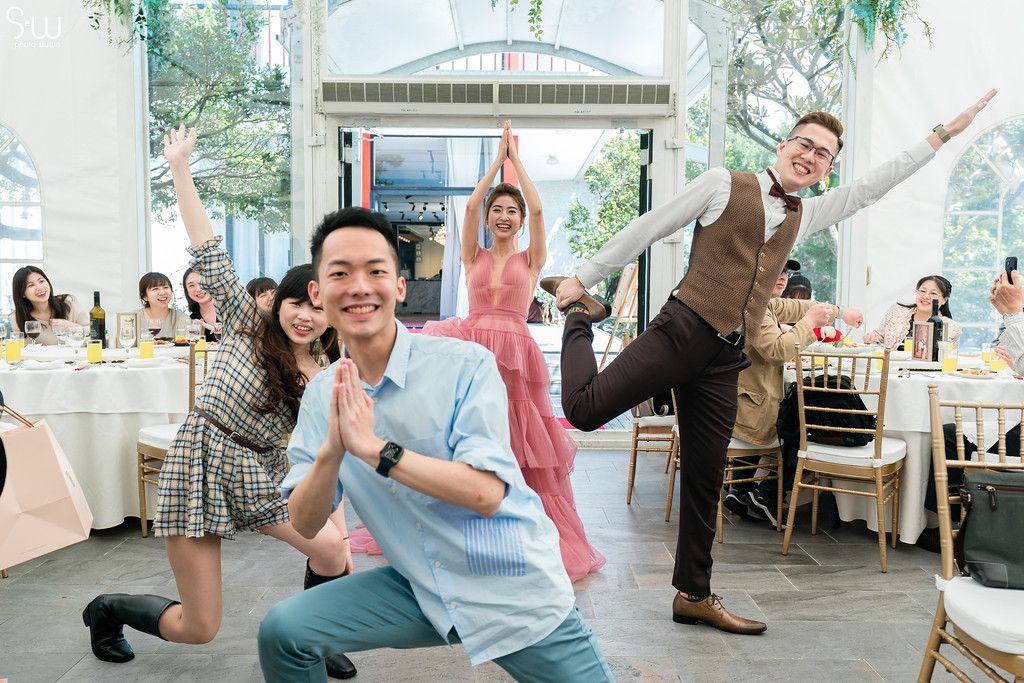 A festive wedding reception shows guests striking playful poses in a tent venue.
