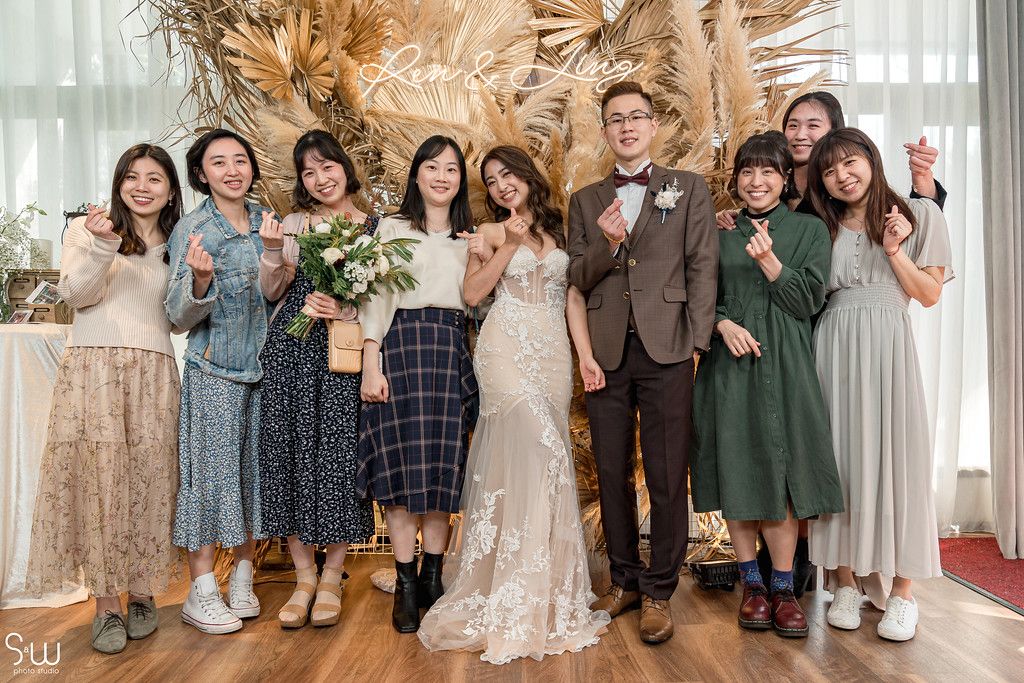Wedding party poses together in front of a neutral backdrop with pampas grass arrangements.