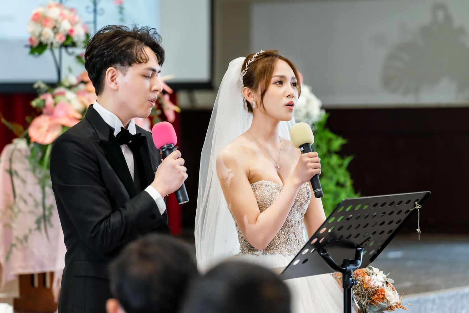 Couple giving speeches at their wedding ceremony with microphones and music stands.