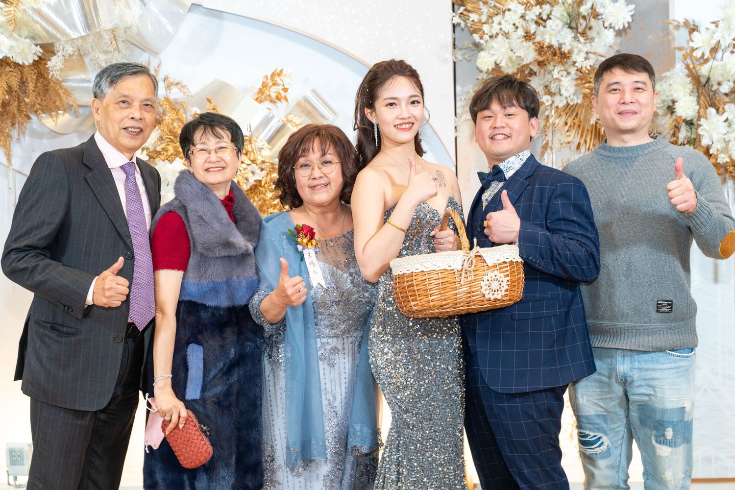 A group of six people celebrate together in formal attire against a white and gold holiday backdrop.