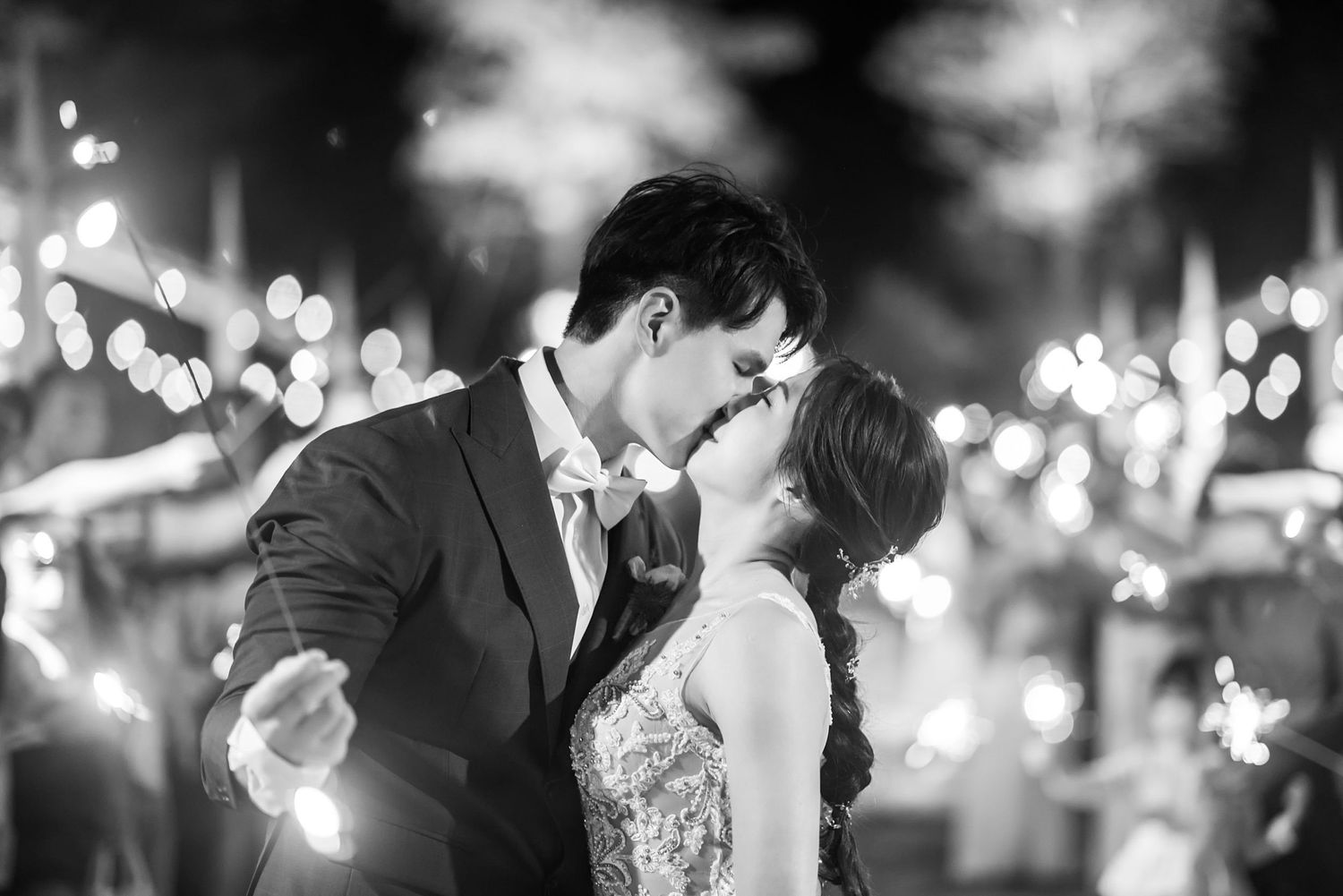 A romantic black and white wedding photo of a couple sharing a tender moment with glowing bokeh lights in the background.