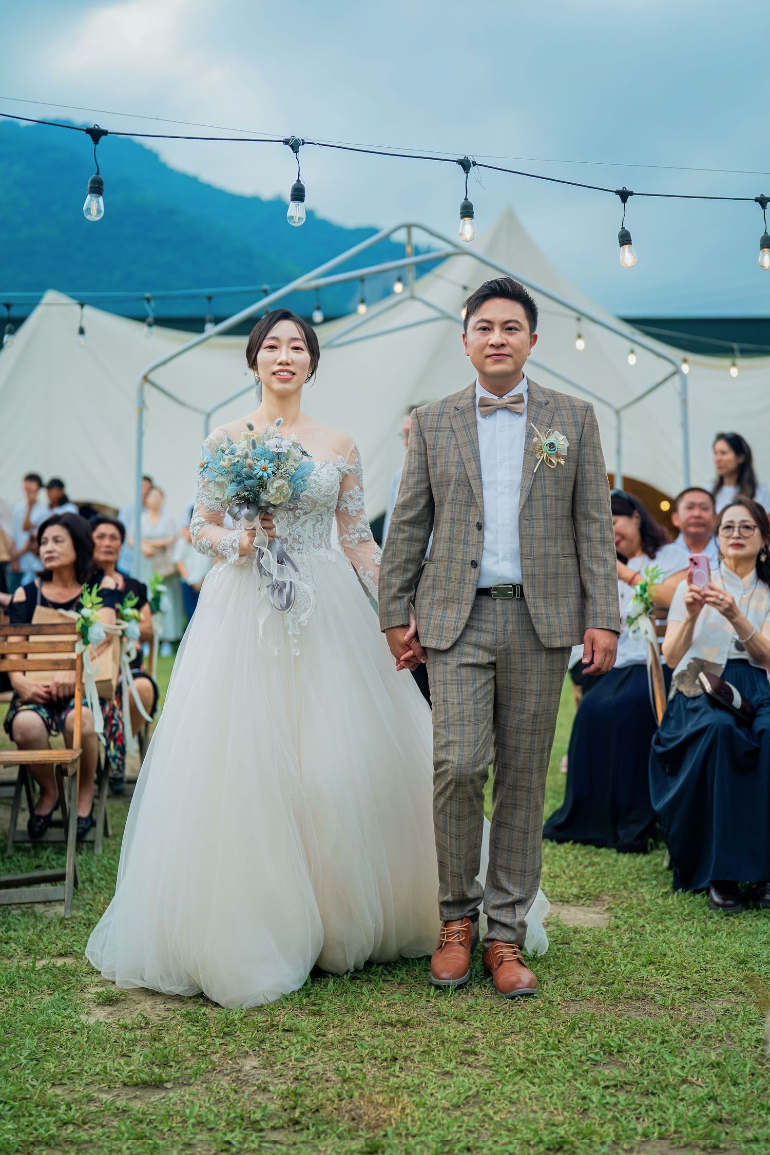 Outdoor wedding ceremony in casual tent setting with string lights and mountain backdrop.