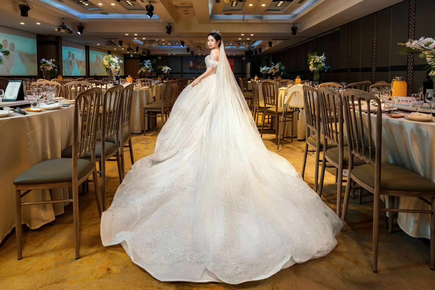 A stunning white ball gown wedding dress with a dramatic cathedral-length train fills an elegant reception venue.