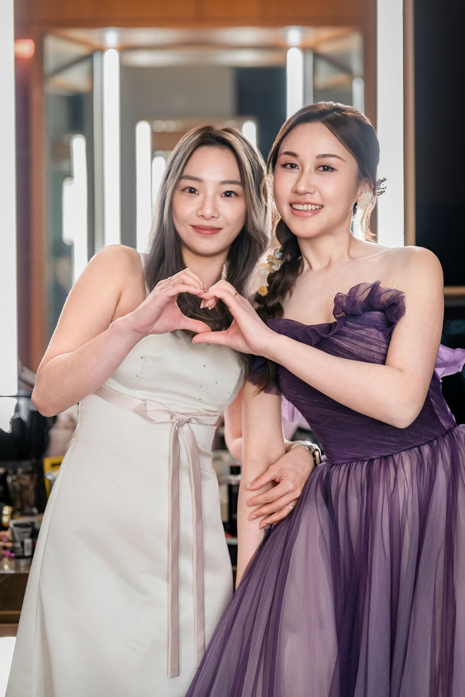 Bridesmaids in white and purple dresses pose together at a wedding venue with bright interior lighting.