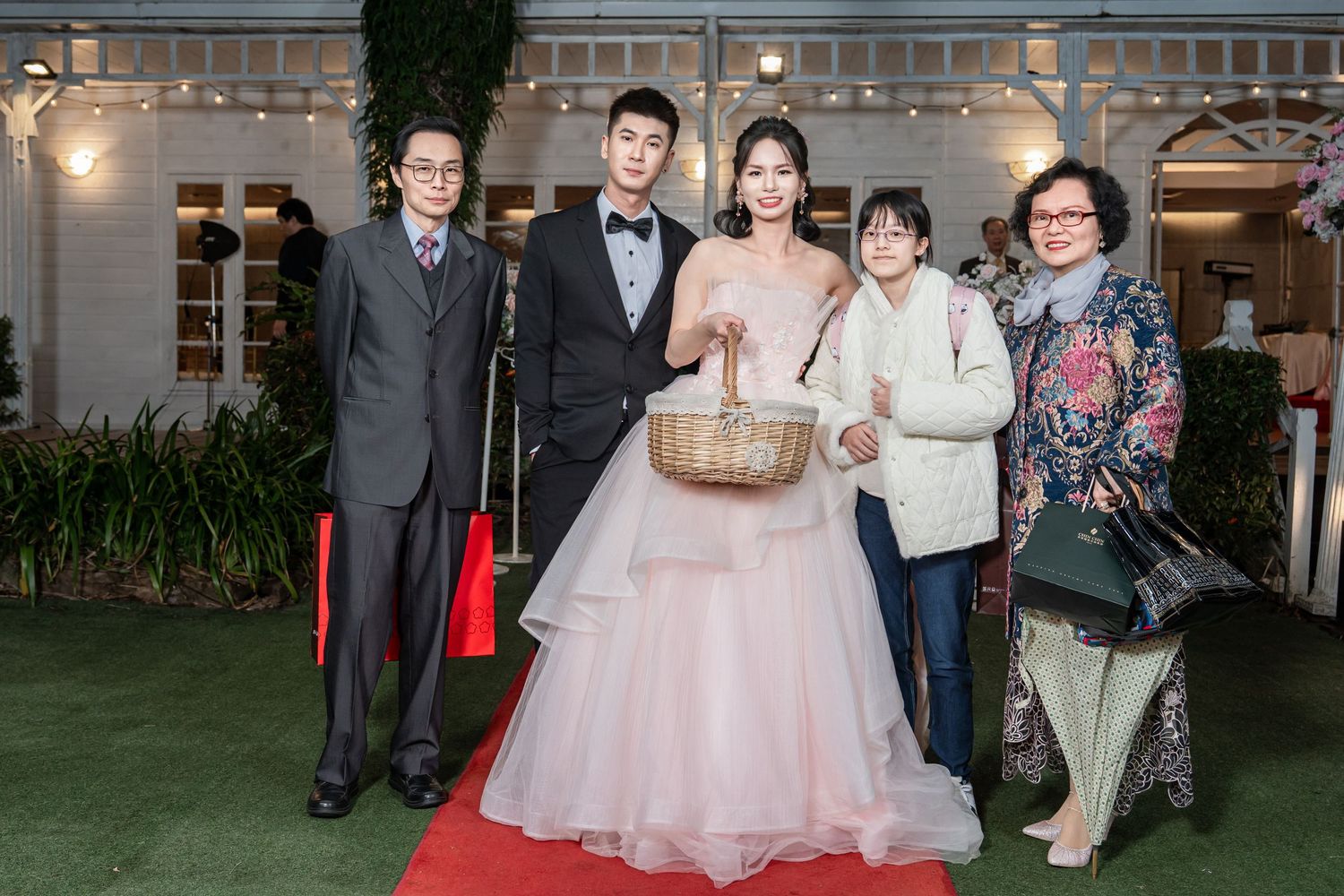 Wedding party guests gather outside a venue in formal attire during an evening celebration.