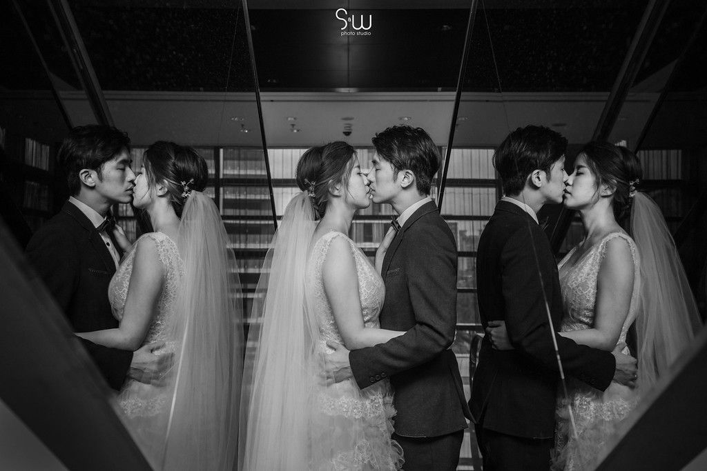 Multiple couples in wedding attire create a symmetrical black and white reflection in mirrors.