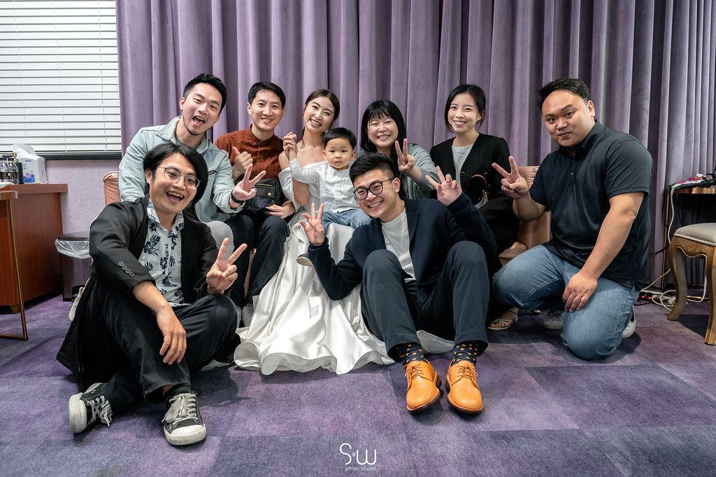 Wedding party members pose casually on purple carpeted floor for a fun group photo.