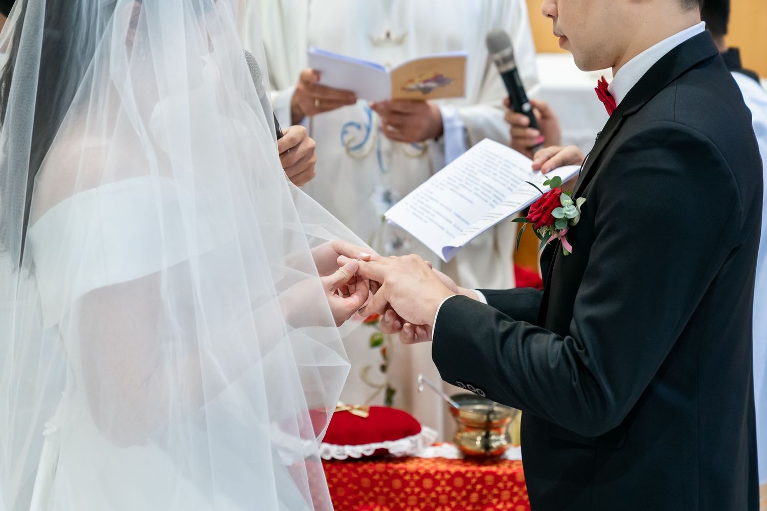 Exchange of rings during wedding ceremony with close-up on hands and white veil details.