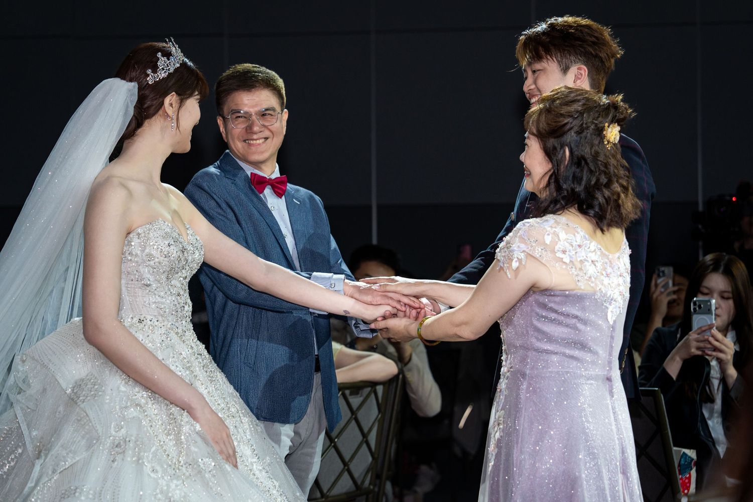 Wedding ceremony with bride in white gown and groom in blue suit joining hands with guests at elegant reception.
