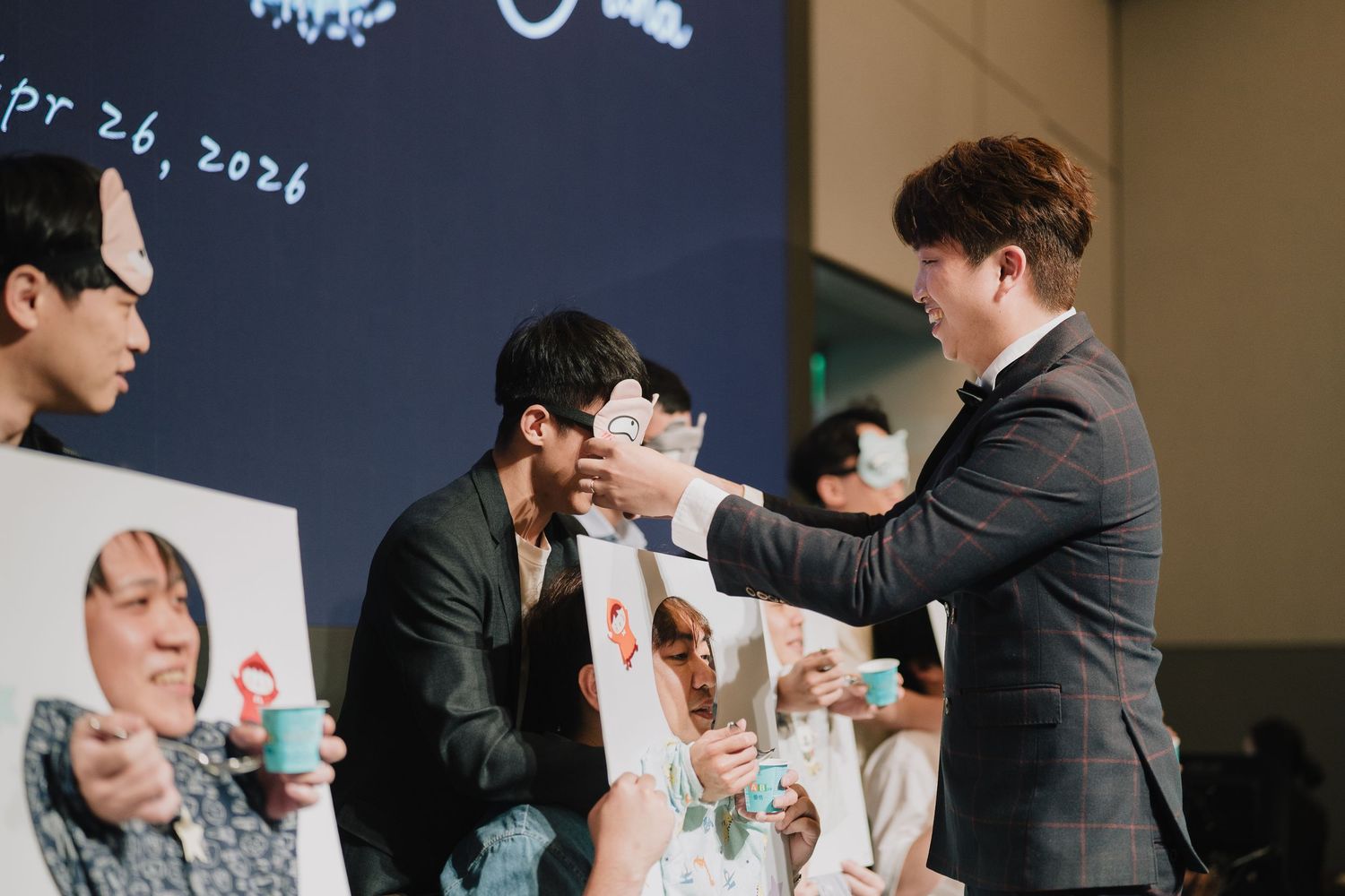 A man in a suit hands items to fans at an event on Apr 26, 2026, with colorful posters displayed in the background.
