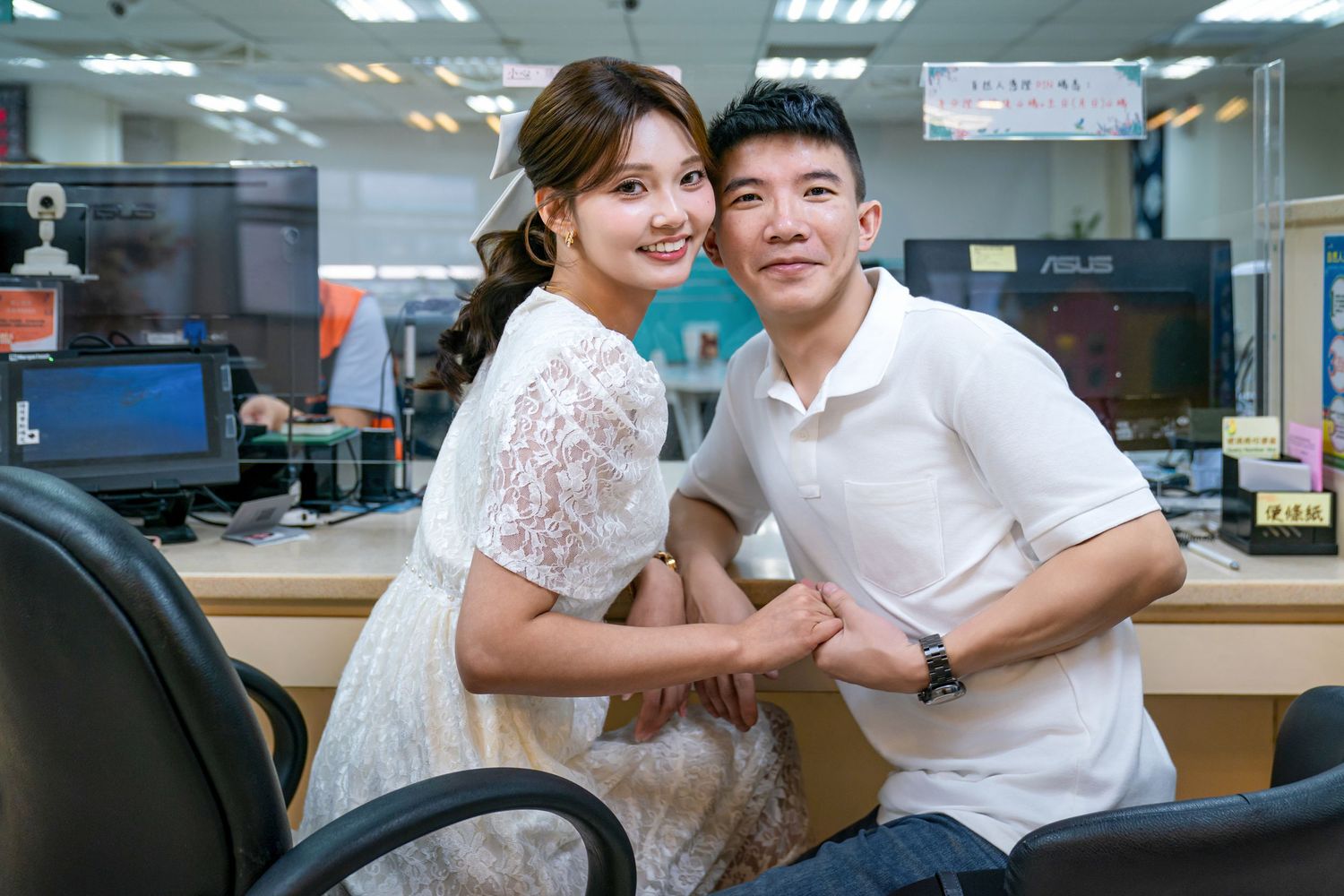 Two coworkers in an office setting share a friendly moment while working at computer desks.