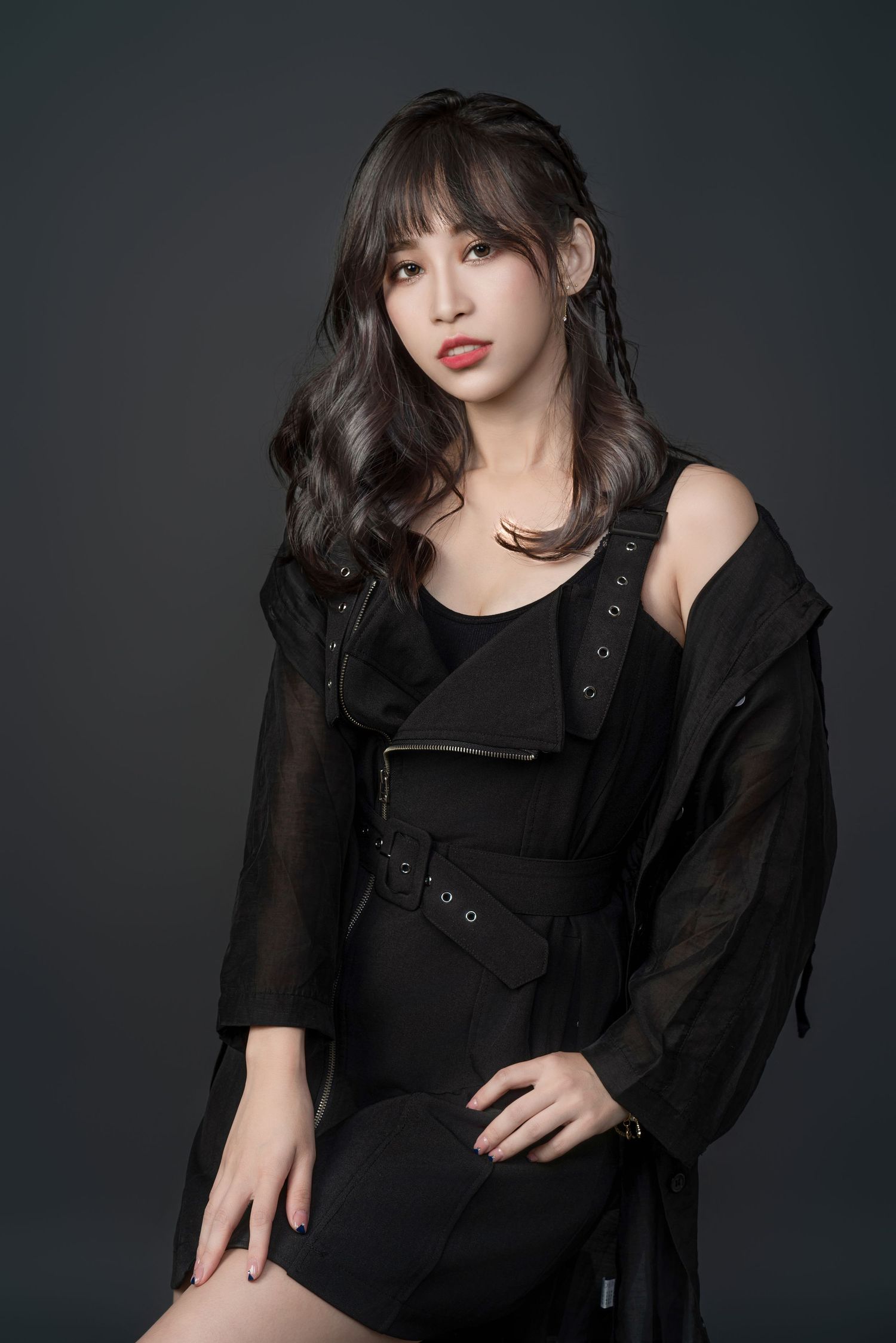 Studio portrait of someone in an all-black outfit with sheer sleeves and dark wavy hair against a dark background.
