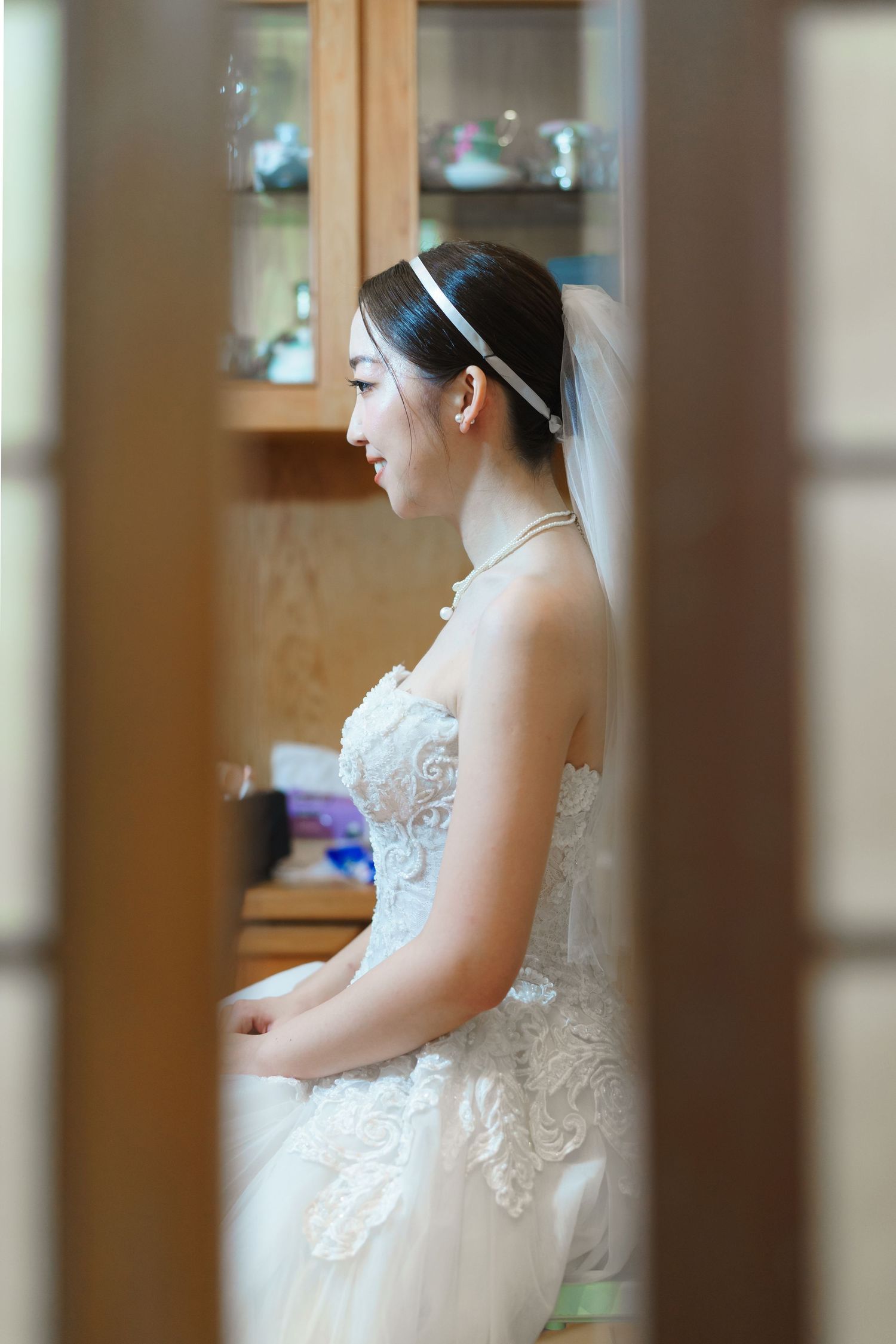 A side profile view of a bride wearing a white lace wedding dress and veil, seen through a doorway.