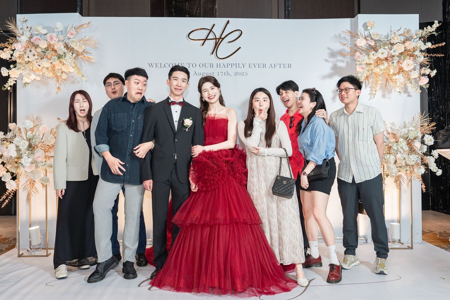 Group photo session at an elegant wedding reception featuring guests in formal attire and a red ball gown.