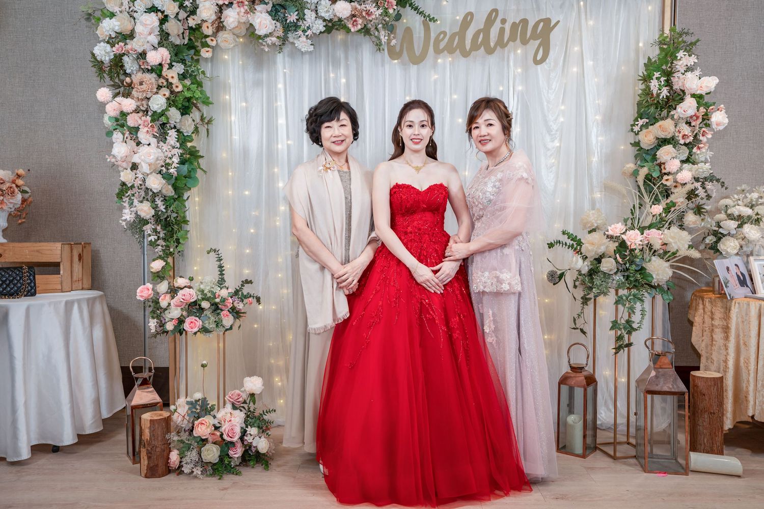 A wedding photo backdrop with pink and white floral arrangements decorating a gray curtain wall.