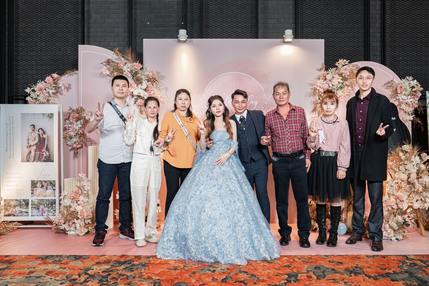 Group photo at an elegant event with floral arch decorations and a person wearing a light blue ballgown in the center.