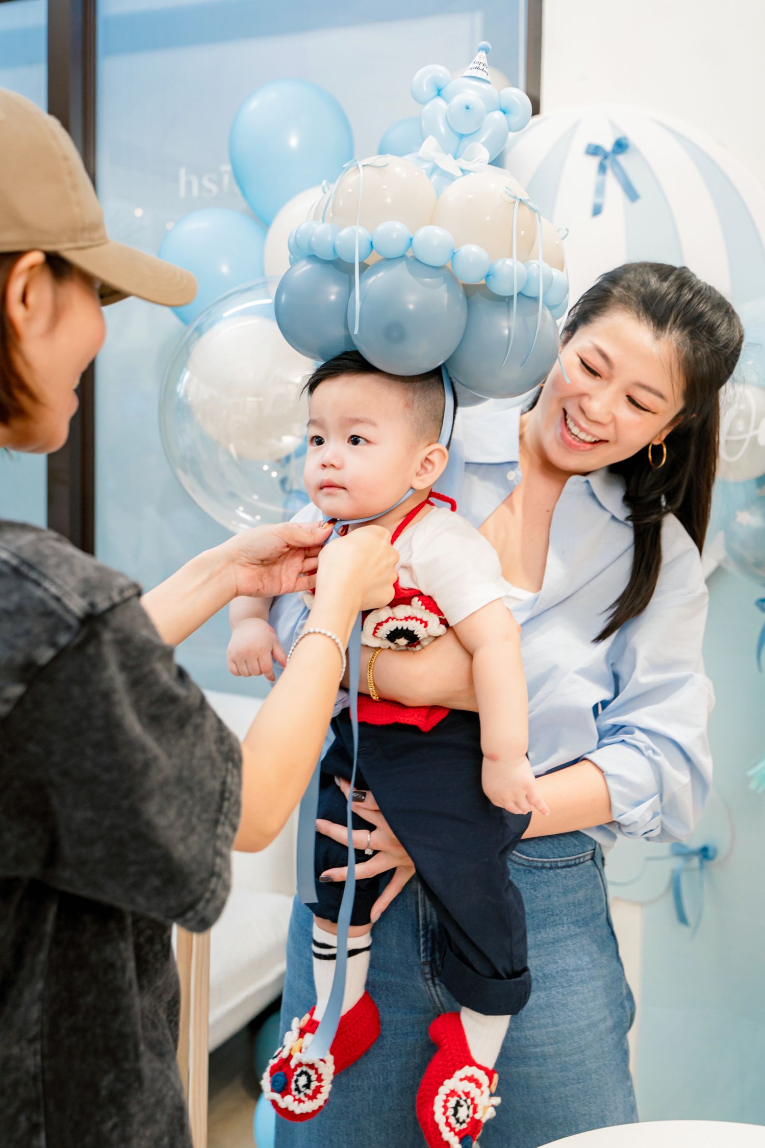 A baby wearing red and navy outfit celebrates with balloons at a festive party with blue decorations.
