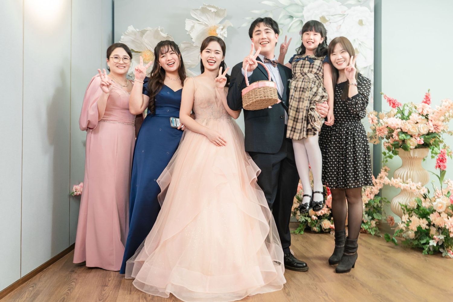 A group poses together at a formal event wearing elegant dresses and suits in pink and navy blue tones.