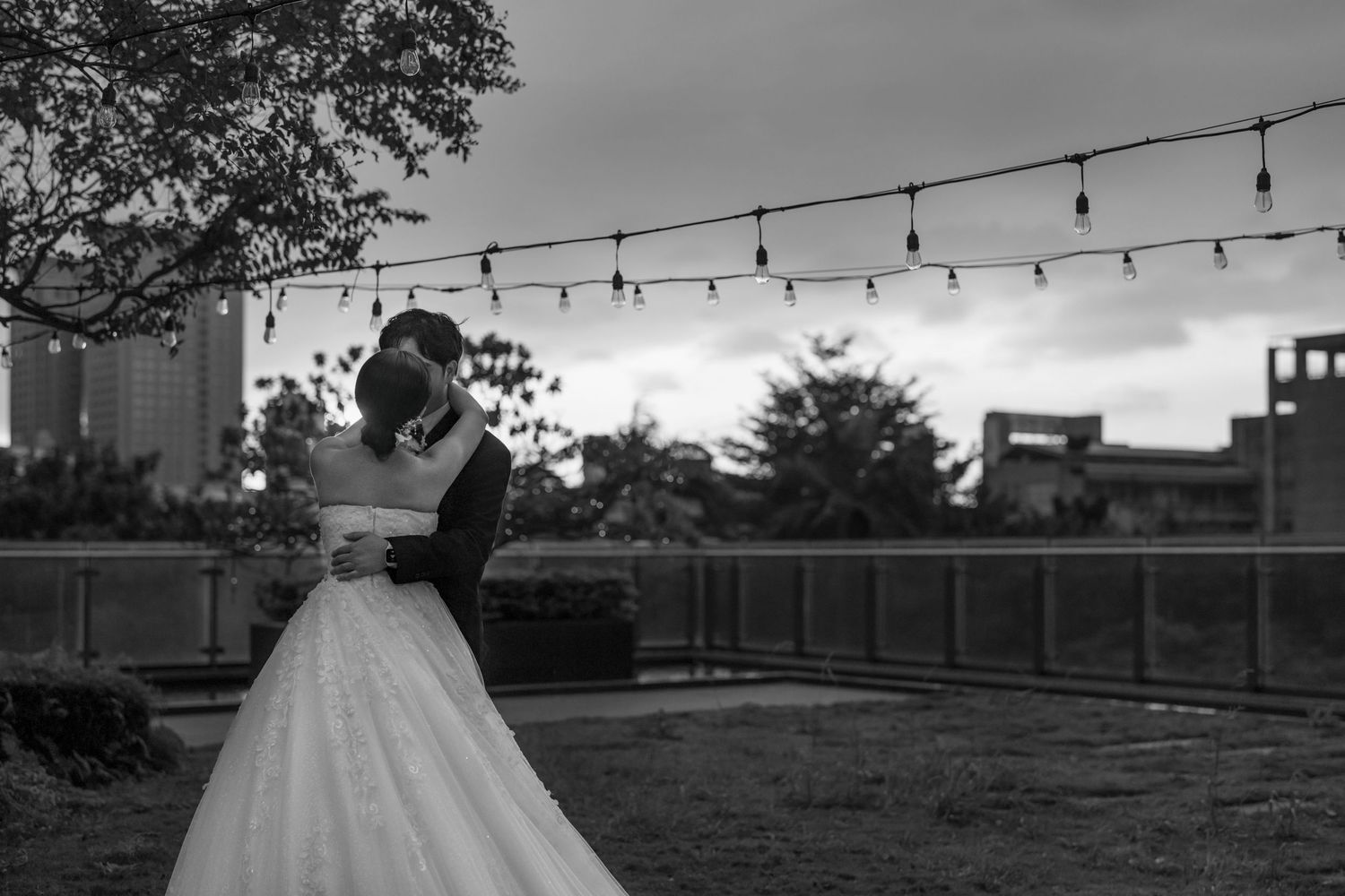 Black and white outdoor wedding ceremony setup with rows of chairs and string lights hanging overhead.