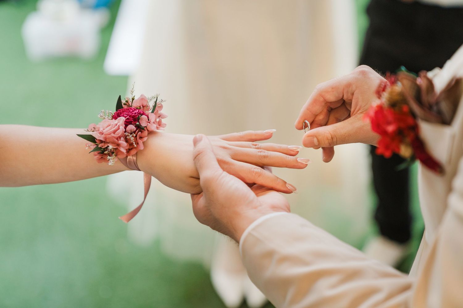 A delicate pink floral corsage being placed on someone's wrist during an outdoor event.