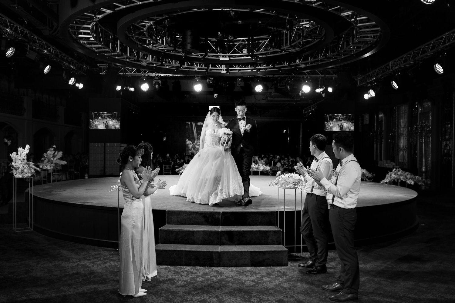 A black and white photograph of performers on a circular stage with dramatic lighting and event decor.