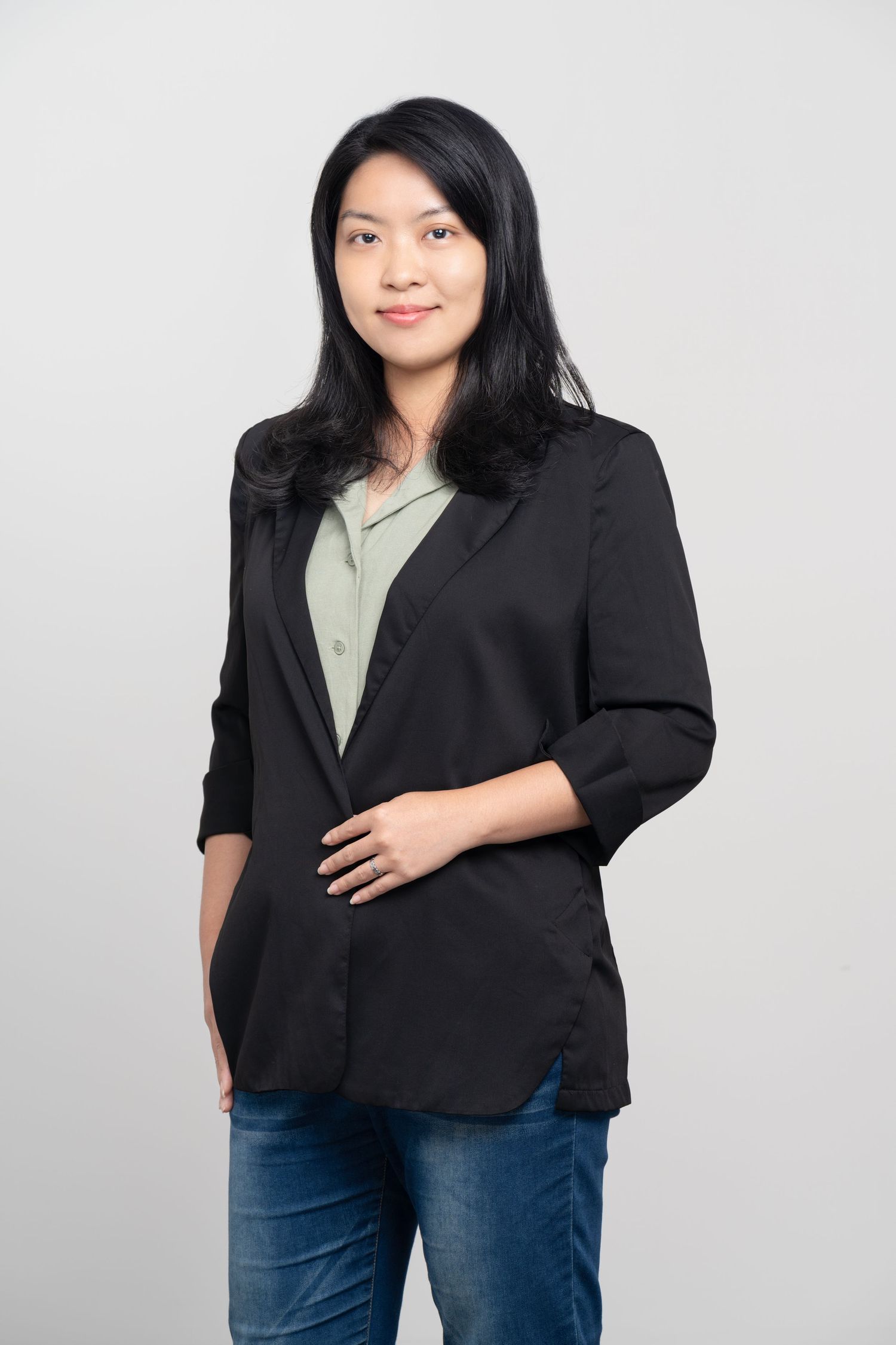 Professional portrait of someone wearing a black blazer and olive shirt against a light gray background.
