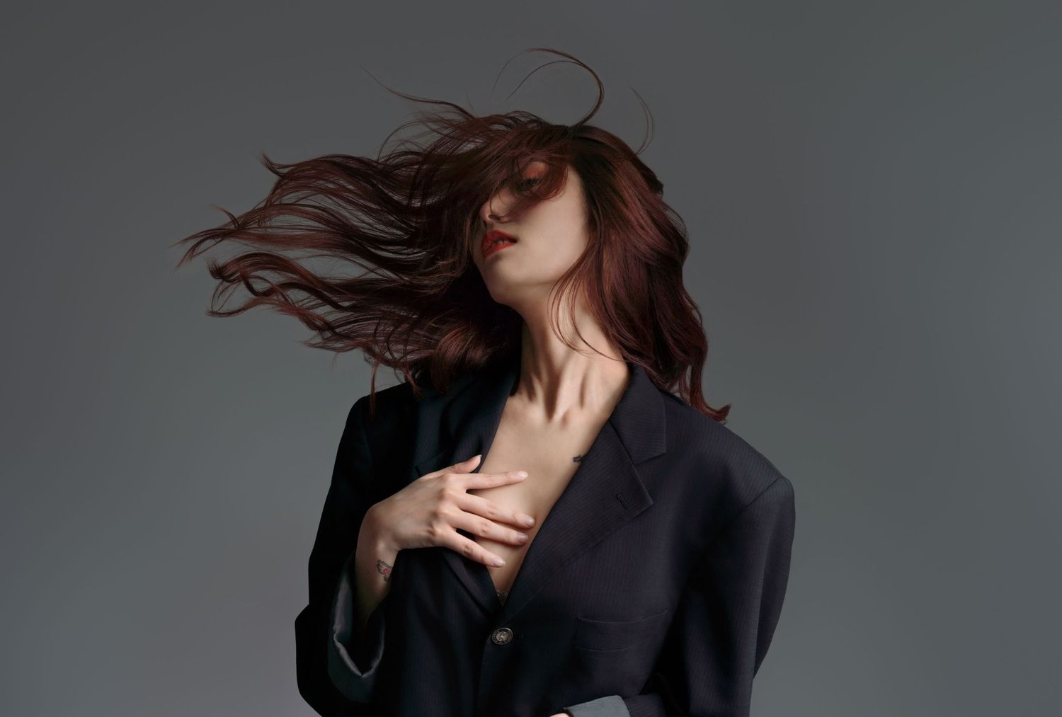 Dramatic studio portrait featuring flowing dark hair motion against gray background in black outfit.