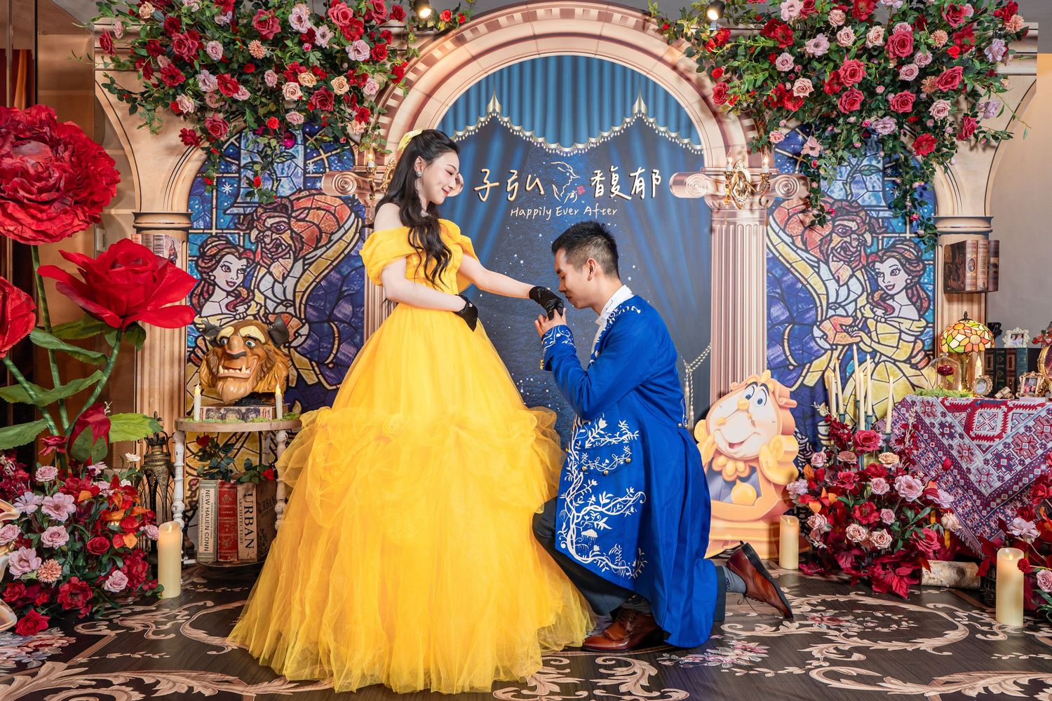 Couple in Beauty and the Beast costumes pose at a floral-decorated engagement celebration backdrop.