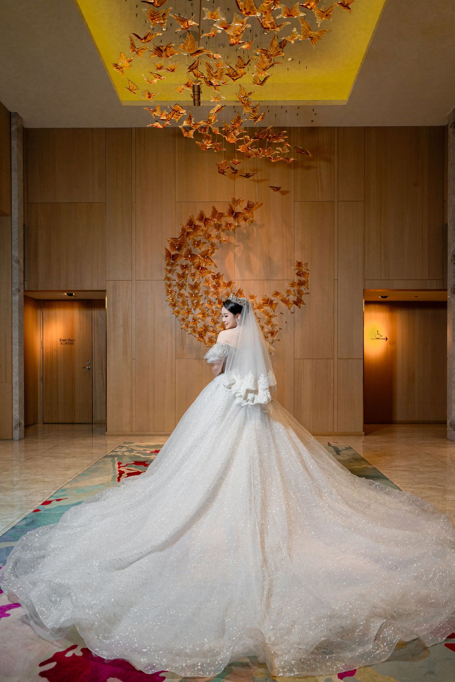 A stunning white lace wedding gown with cathedral-length train is photographed in a warm-lit hallway with autumn decor.
