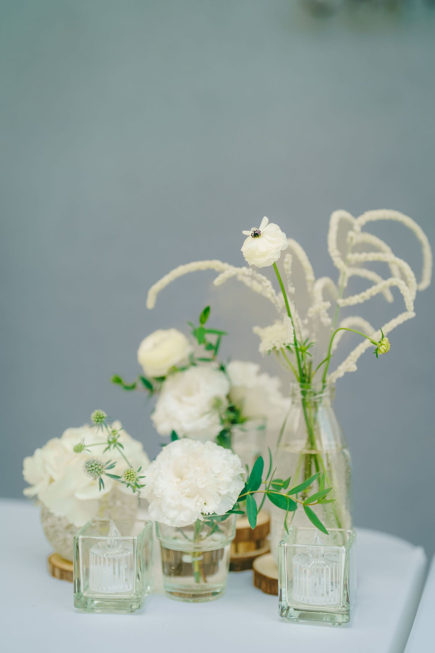 Small glass vases filled with delicate white flowers and greenery create an elegant minimalist table arrangement.